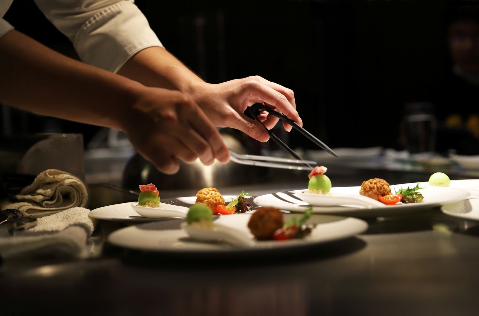 Close-up of a professional chef using precision culinary tweezers to plate high-end hors d'oeuvres, illustrating the technical mastery required for Private Chefs Inc. candidates.