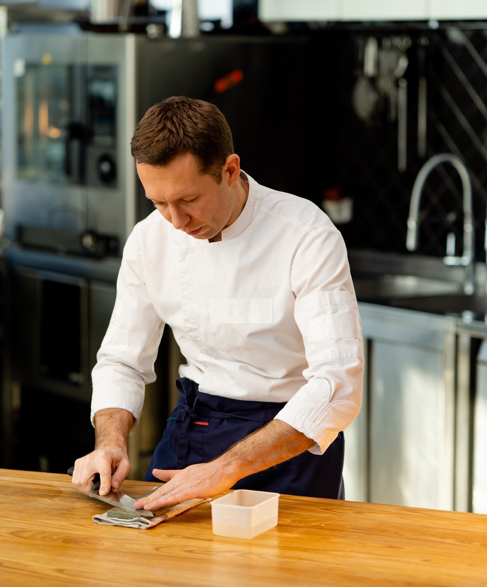 A skilled chef focused on sharpening a steel blade, symbolizing meticulous preparation and culinary mastery