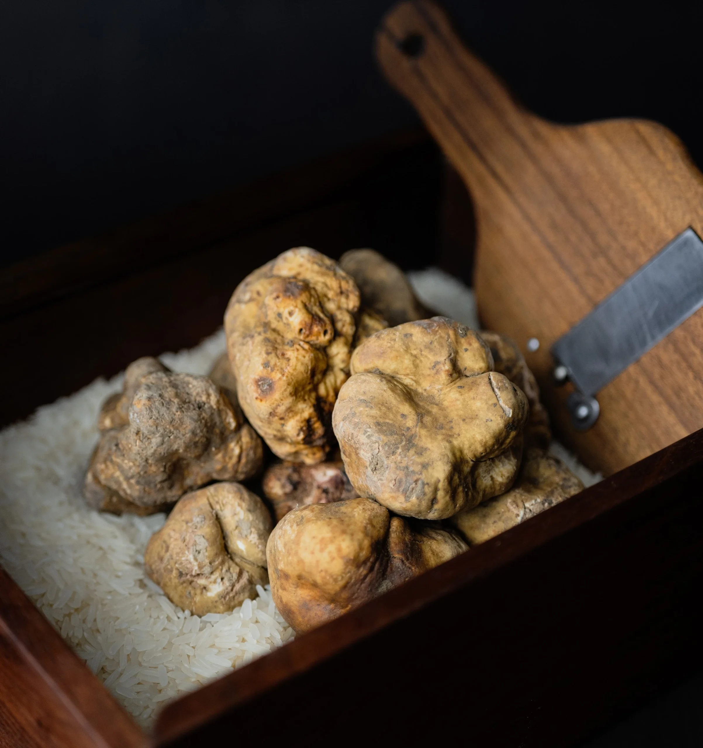 Premium whole white truffles displayed with a professional wooden truffle shaver, showcasing elite ingredient sourcing and culinary provisioning.