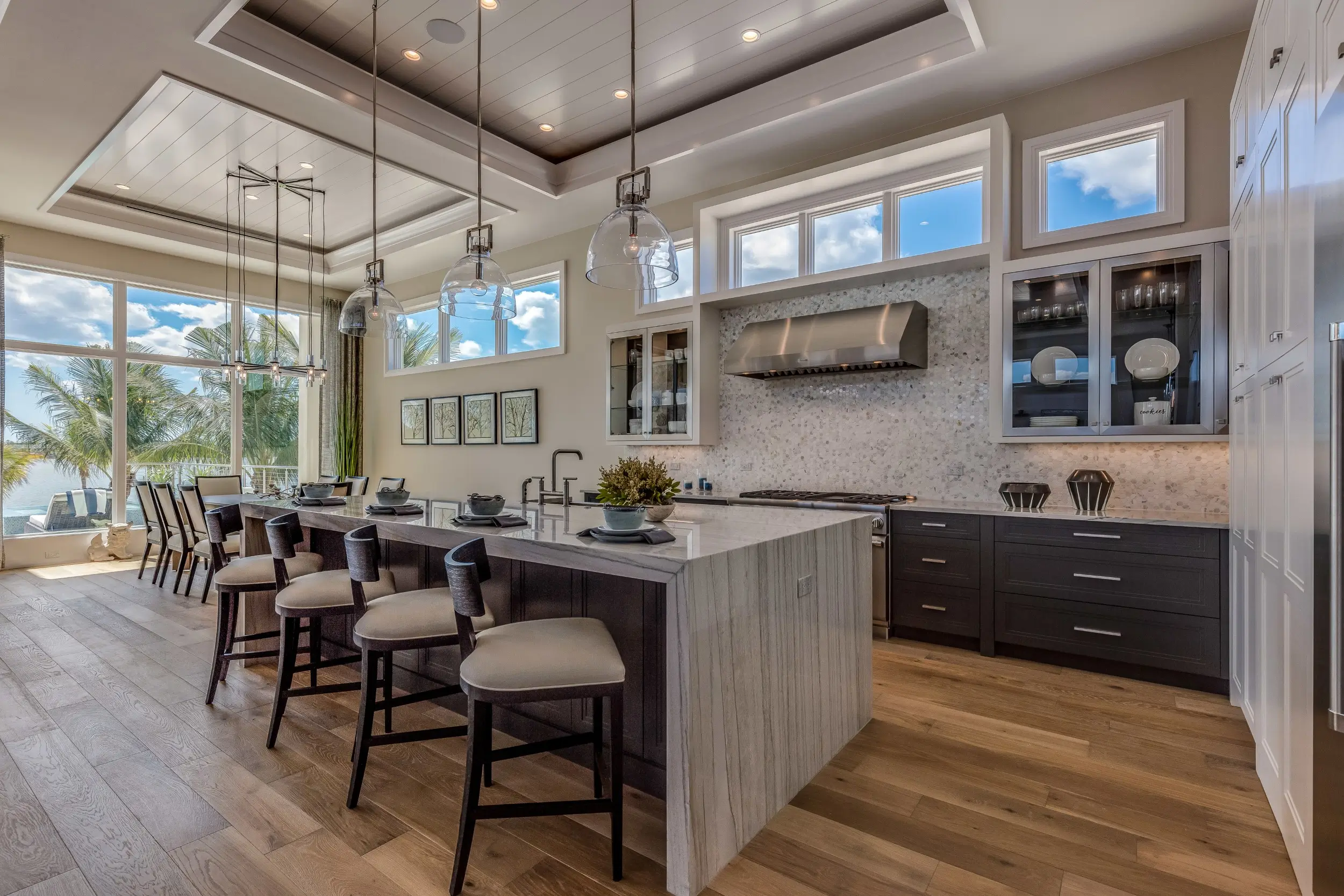 Ultra-luxury modern estate kitchen in Palm Beach with dark cabinetry and tropical palm trees visible through large windows, symbolizing the culinary engine of a South Florida residence.