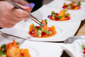 A close-up of a Michelin-caliber chef using precision tweezers to plate an intricate lobster dish with edible flowers and fresh vegetables, showcasing technical culinary artistry