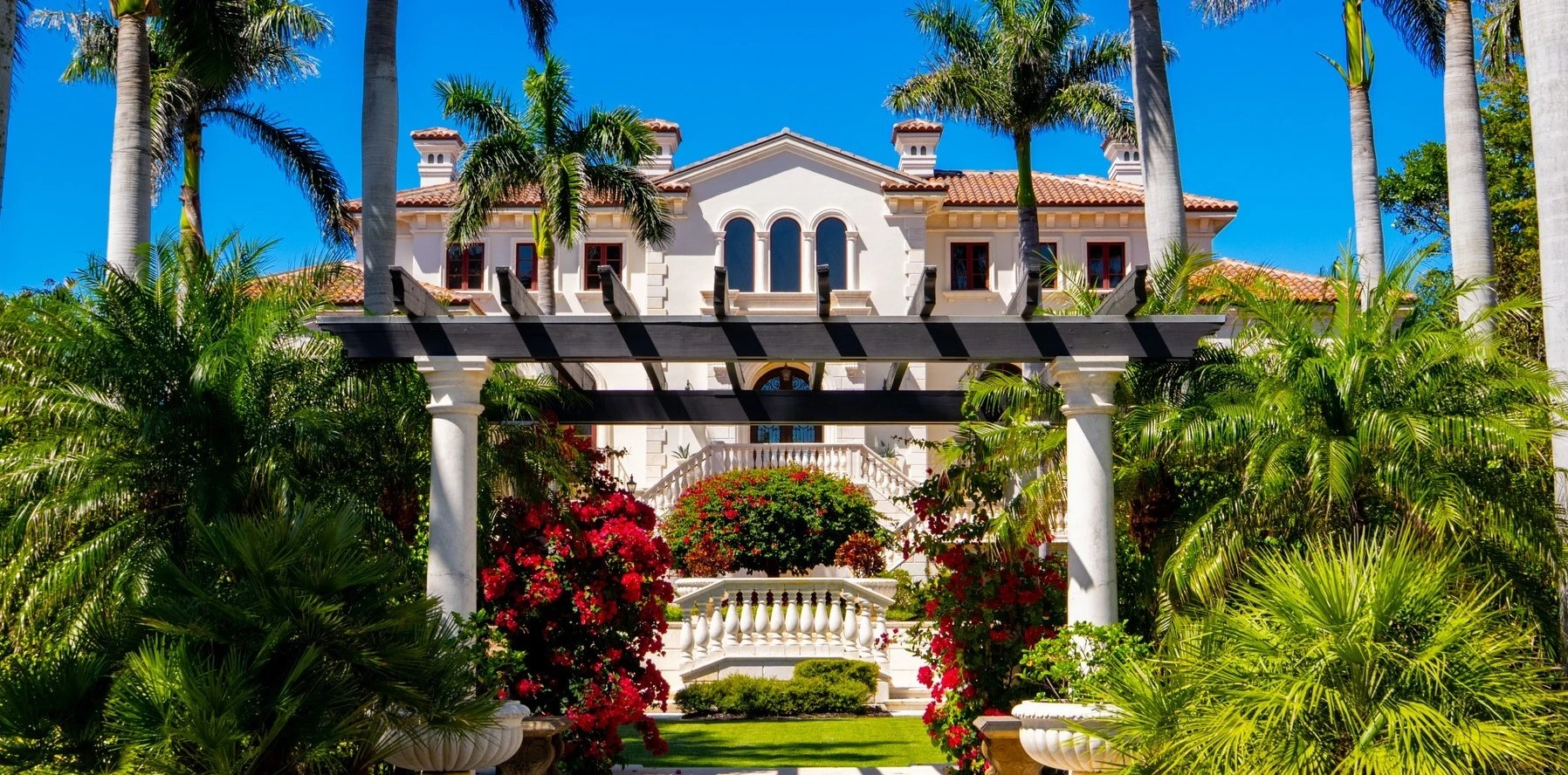 A luxury Mediterranean-style waterfront estate with lush palm trees and a white pergola, representing seasonal placement locations for private chefs.